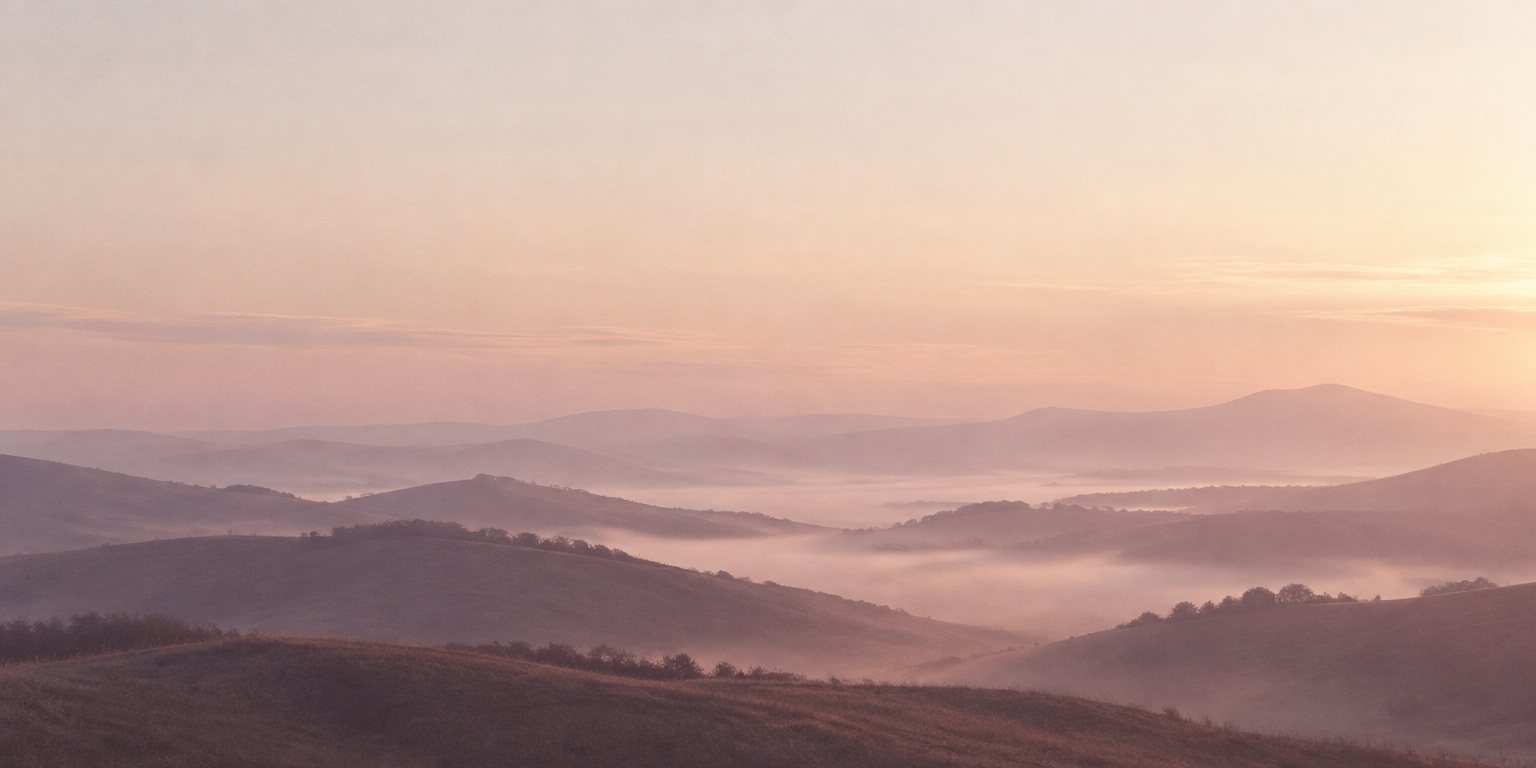 Sanfte Hügel im Morgennebel, in Malve und Rosé, darüber ein weiter, heller Himmel